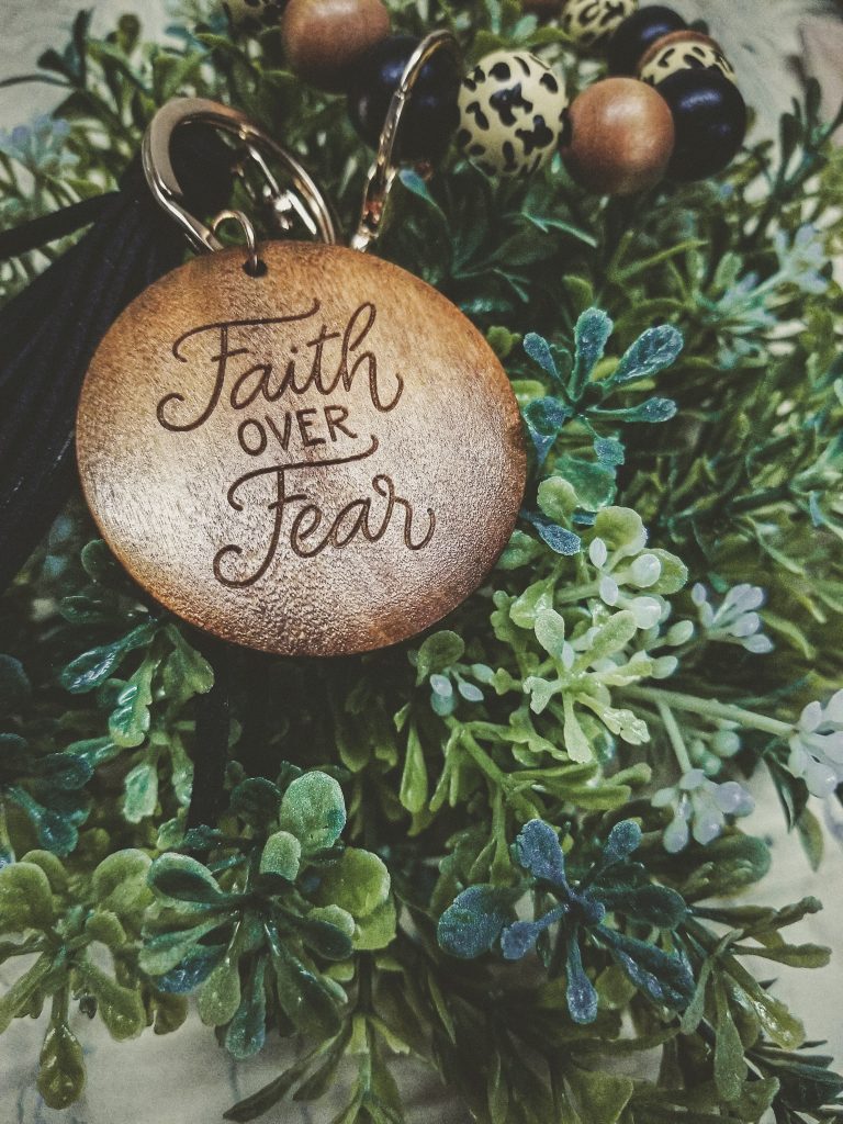 Wooden keychain with the words "Faith over Fear" on top of greenery