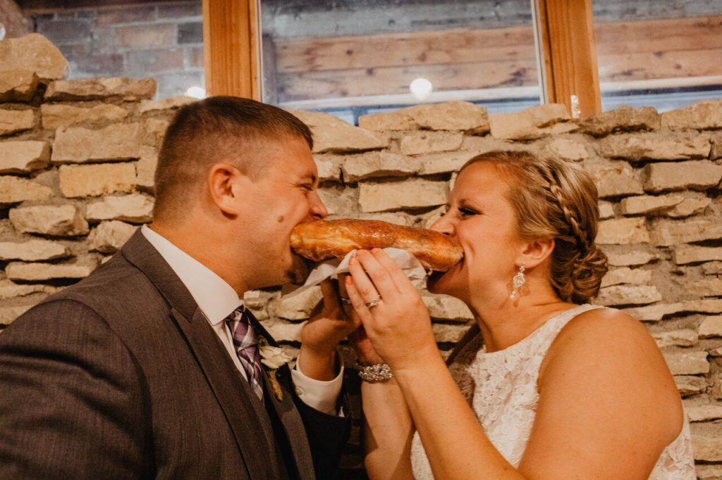 groom on the left, bride on the right taking a bite of a giant donut