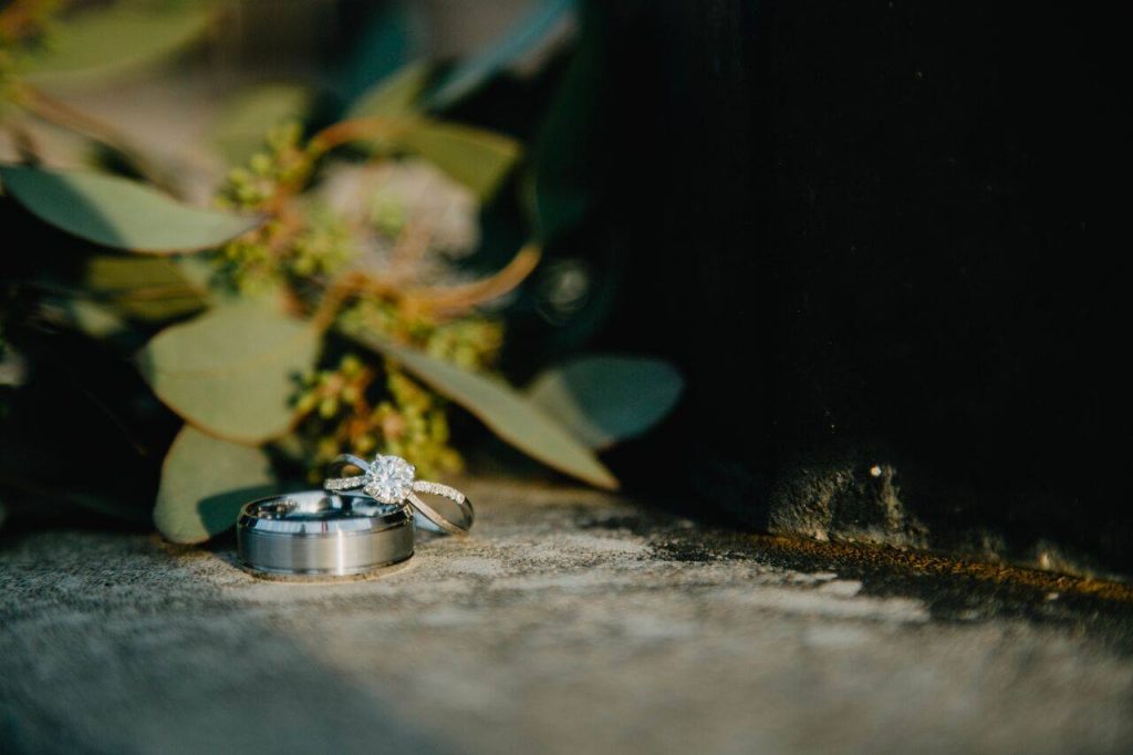 Men's wedding band and woman's wedding ring in front of greenery on a stone table. 