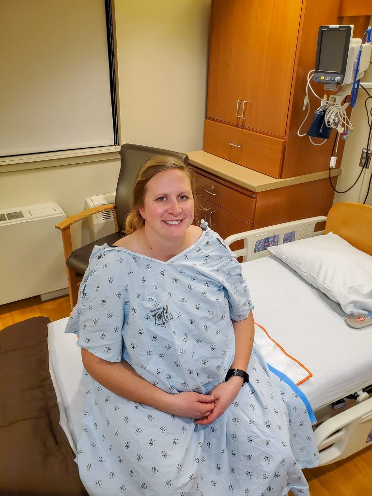 Pregnant woman in blue hospital gown sitting on hospital bed