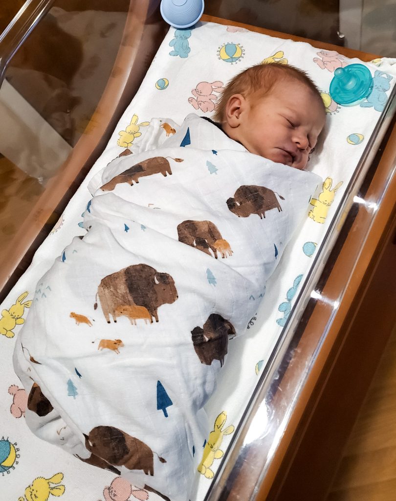 Newborn baby in hospital basinet with buffalo print blanket