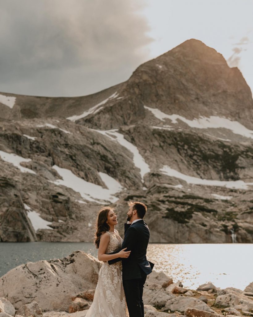 Bride on the left, groom on the right in front of mountains smiling. 