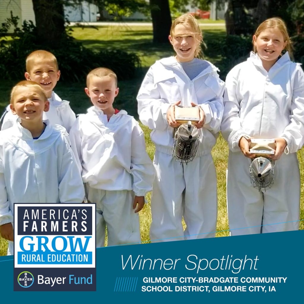 Students wearing white beekeeping suits, holding two bee smokers with the words America's Farmers Grow Rural Education Bayer Fund Winner Spotlight Gilmore City-Bradgate Community School District, Gilmore City, Iowa