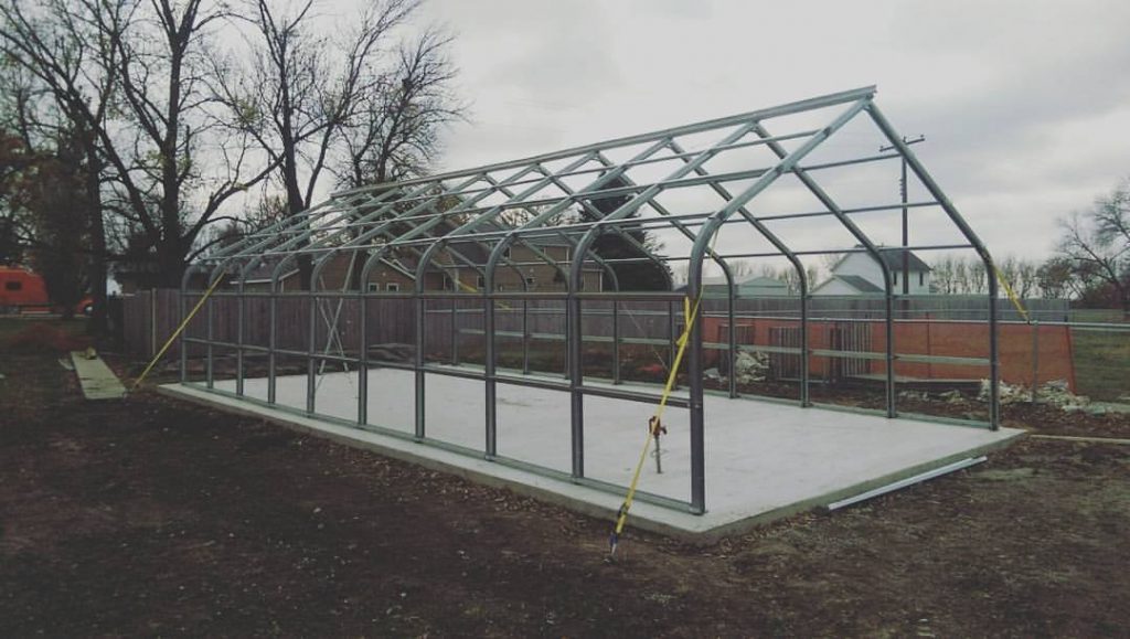 Metal greenhouse structure on concrete pad, with rachet straps holding down frame. 