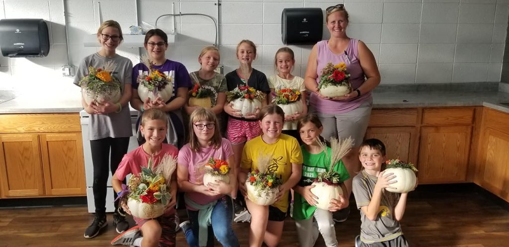 Five students in front row holding decorated white pumpkins with five students in back row with teacher on the right holding white decorated pumpkins