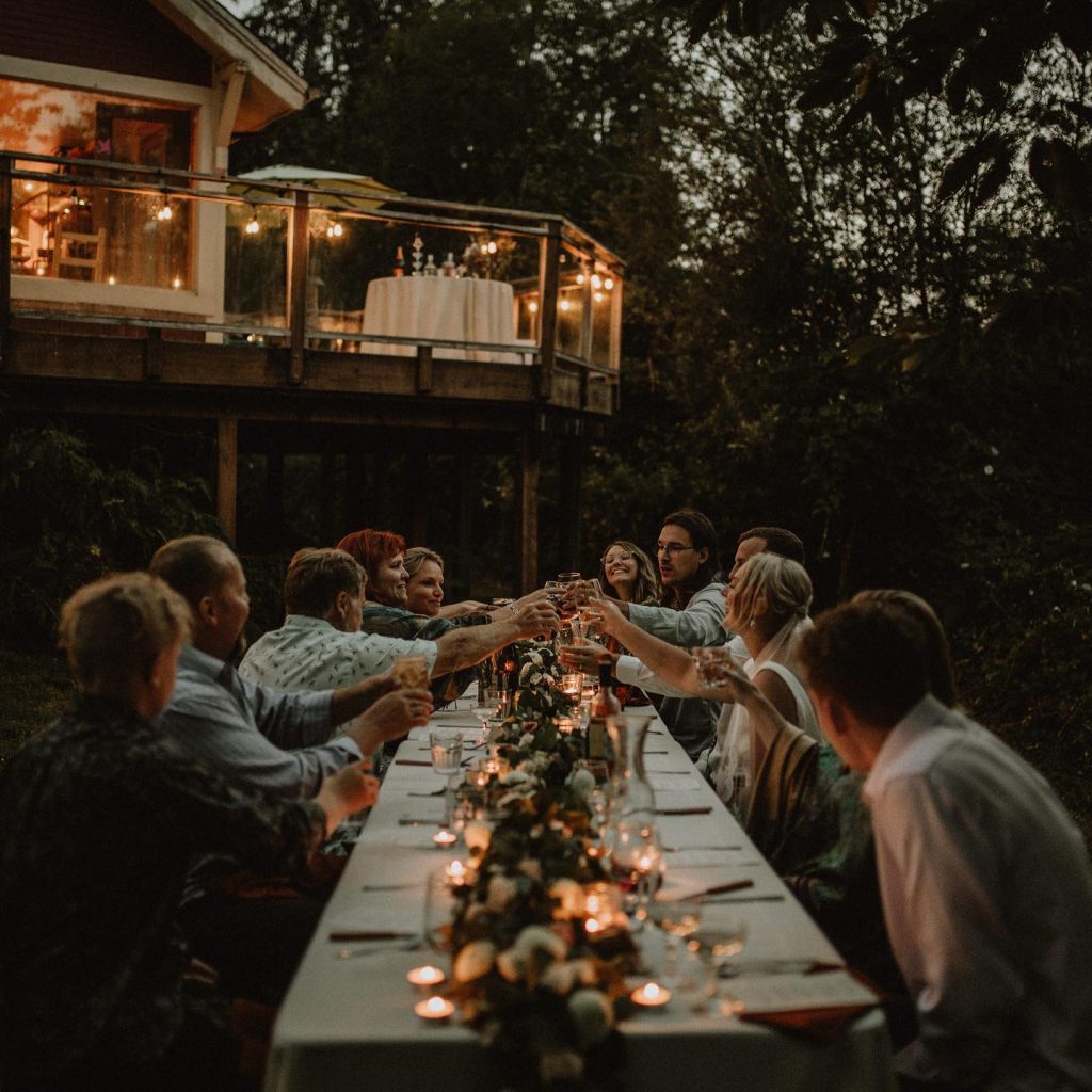 Wedding party making a toast together over a candlelit table with a white table cloth surrounded by trees. 