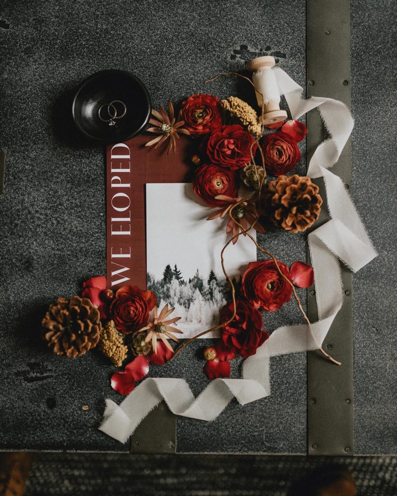 Red flowers, white ribbon, and pine cones sitting on top of a picture frame that says "We Eloped."