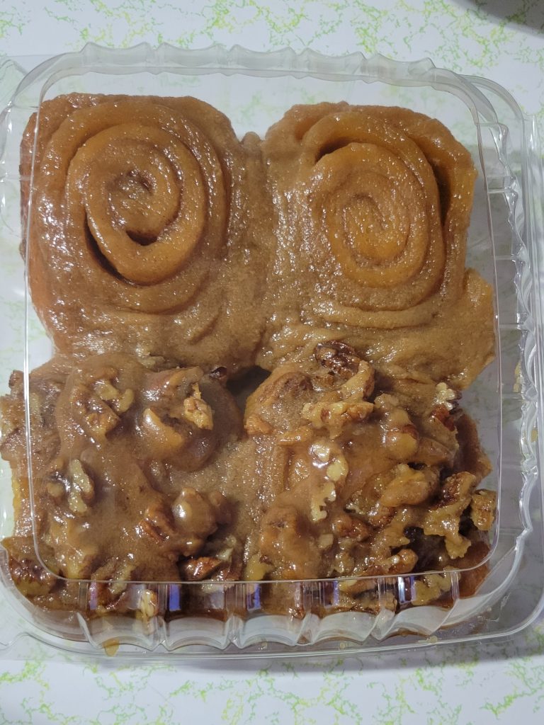 two cinnamon rolls on top and two pecan rolls on the bottom in a plastic clamshell container. 